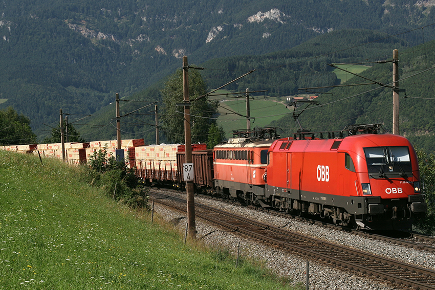 Roter Güterzug der ÖBB Rail Cargo Group auf einer Bahnstrecke vor grüner Bergkulisse.
