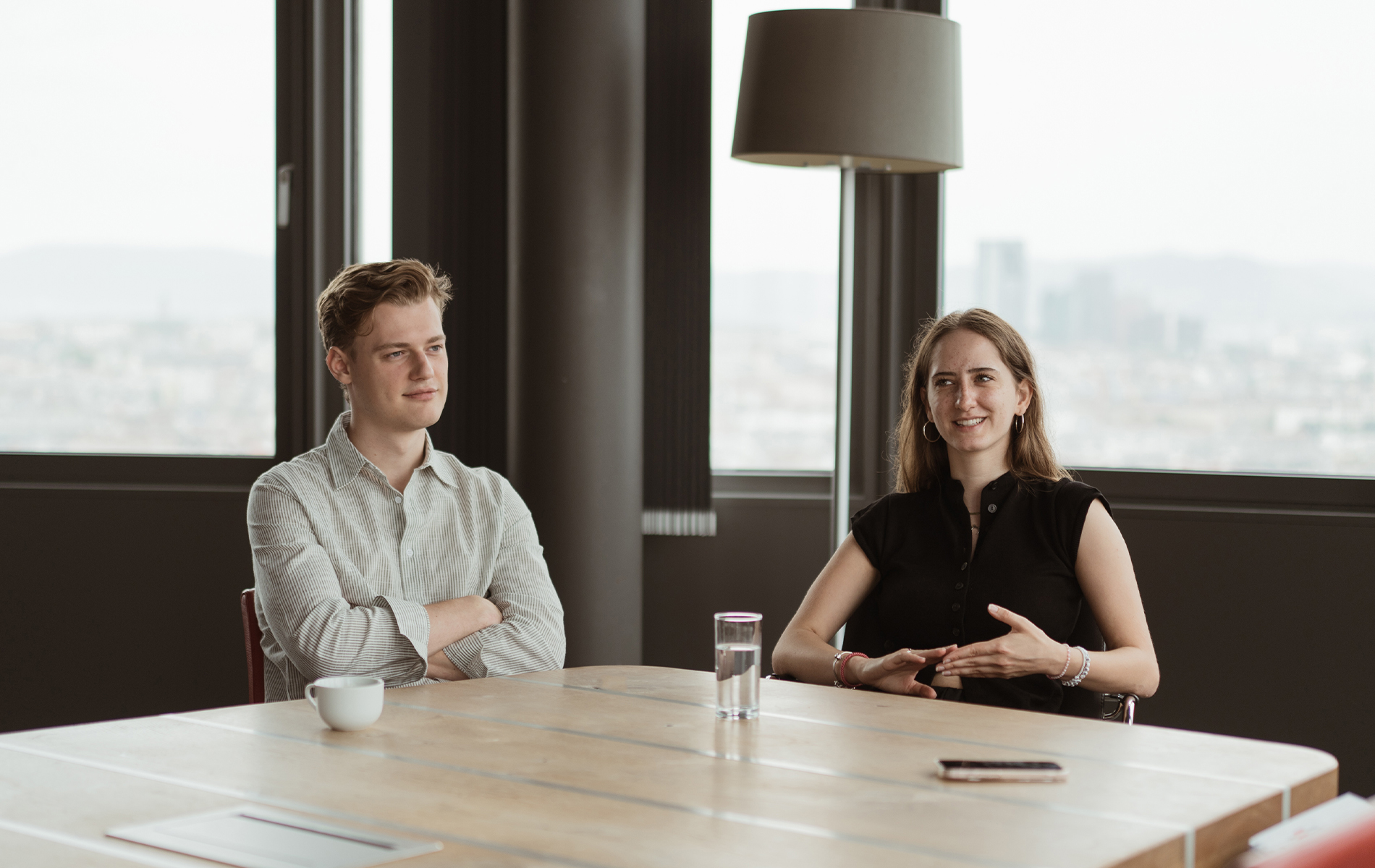 Praktikant:innen Laura und Konstantin sitzen an einem Besprechungstisch im Büro.