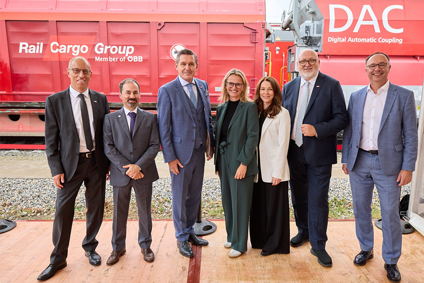 Group photo of participants in front of Rail Cargo Group freight wagons and the DAK exhibition area.